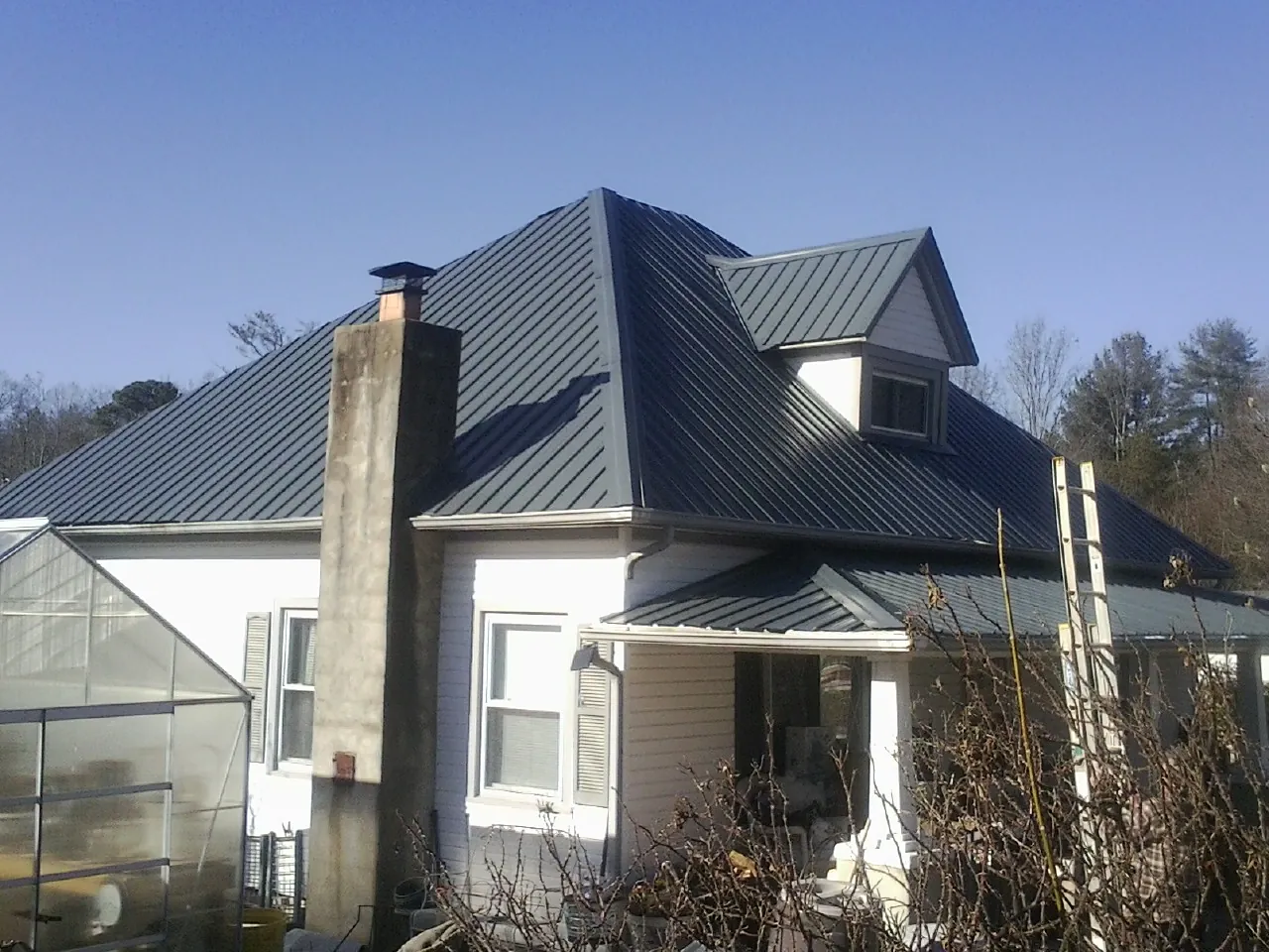 Dark blue standing seam metal roof on a white farmhouse with dormer — Slate & Tile Roof Repair by Roofing Brothers in Pelzer