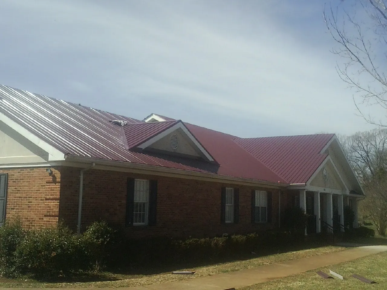 Red metal roof with gabled entries on a long brick building, from a Hail Damage Roof Repair job in Pelzer