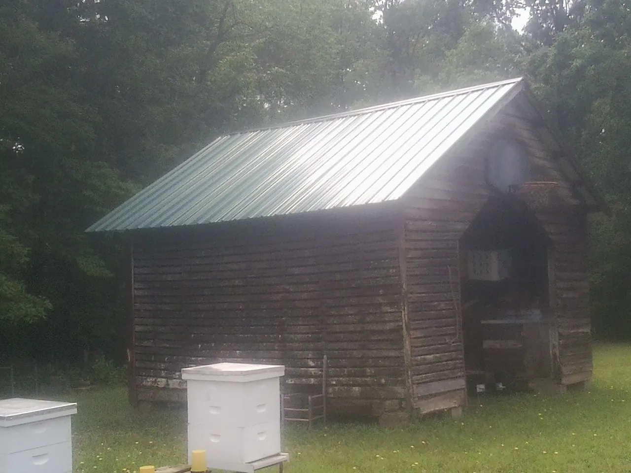 Green metal roof on a weathered barn beside stacked beehives in Pelzer