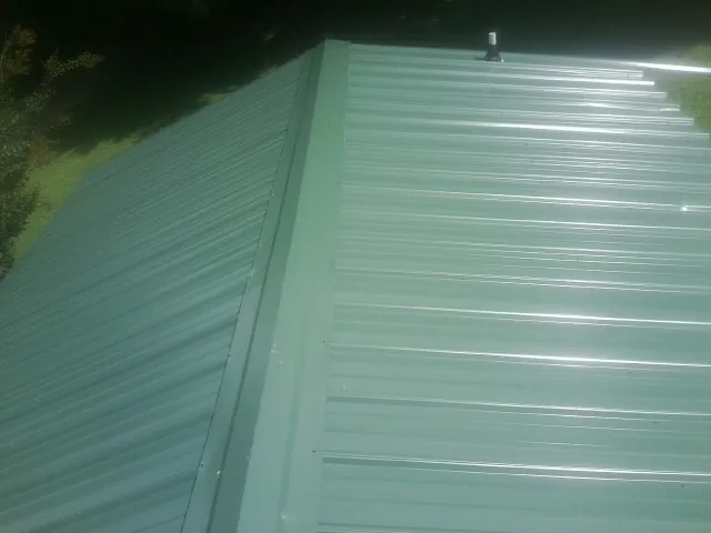 New green metal panels meeting at the ridge of a roof — Flat Roof Repair work by our crew in Pelzer