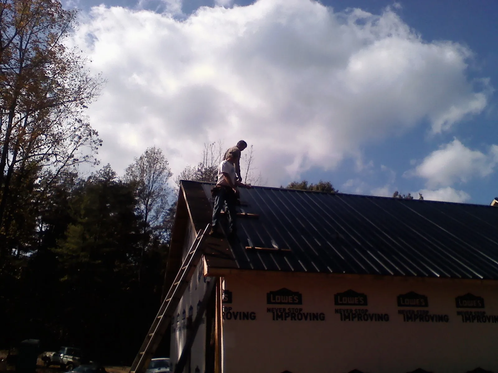 Roofer fastening dark metal panels high against a cloudy sky, from a Roof Inspection job in Pelzer